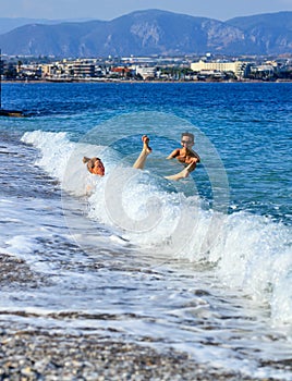 A coastal wave knocks down a young lady who enters the sea by a pebble beach