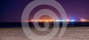 The coastline of Blankenberge beach lighted by night, colorful lights on the industry terrain in the distance