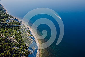 Coastline with blue sea, cliff with pine trees and motor boat. Summer da. Aerial view