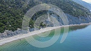 Coastline with blue sea, cliff with pine trees and motor boat. Summer day on quiet sea. Aerial view