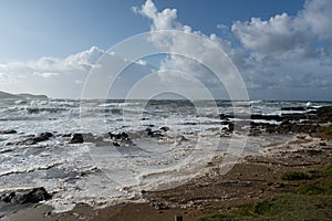 Coastline with rocks, a blue sky and rough incoming waves with sea spray during a storm