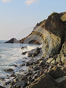 Coastline with rocks and cliff, a blue sky and incoming waves with sea spray in summer