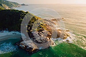 Coastline with rocks and ocean with waves at warm sunrise in Brazil. Aerial view