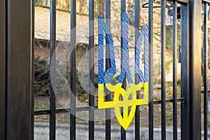 Coat of arms of ukraine in blue and yellow on a black metal fence.