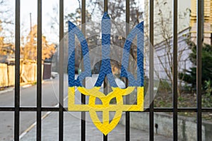 Coat of arms of ukraine in blue and yellow on a black metal fence.