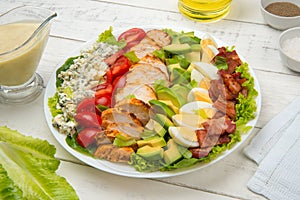 Cobb salad in a white salad bowl with ingredients on an old rustic white wooden table.