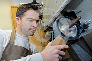 Cobbler holding sole shoe against rotating wheel