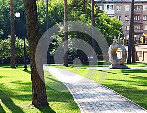 A cobblestone alley near in the middle of tall tree trunks in the summer. Green lawn