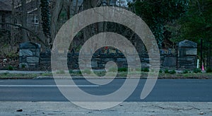 A Cobblestone Wall Across a Blacktop Street With a Dead Forest Behind It