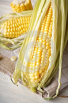 Cobs of ripe raw corn on white wooden background, close-up