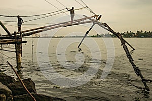 Cochin, India - 20 august 2019: fishermen stand on traditional chinese fishing nets in early morning with warm natural soft light