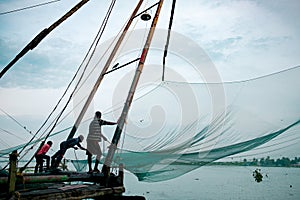 Cochin, India - 20 august 2019: indian fishermen stand on traditional chinese fishing nets structure  in early morning with warm