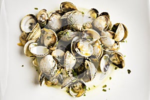 Cockles cooked with parsley and half a lemon on a white plate