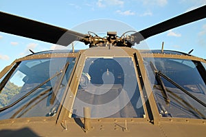Cockpit windscreen of a olive drab military helicopter against a blue sky