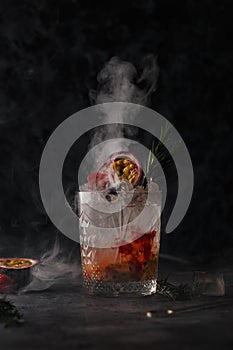 Cocktail in a bar on a dark background in smoke and steam. Alcoholic shot with fruit and ice.