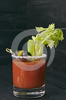 Cocktail Bloody Mary with lime and celery, salt and snacks in a glass on a black wooden table. vertical view of a cocktail