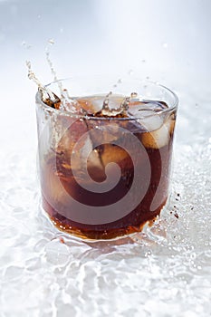 cocktail with cola and ice in a transparent glass with beautiful splashes