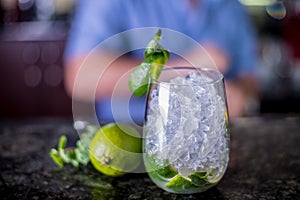 Cocktail decorated with mint and a slice of lime, grass with ice in a glass of wine Balon with bartender on background