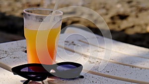 Cocktail drink on the beach. Sunglasses, holiday, relaxed. Close up glass of smoothie juice and sunglasses on sand at