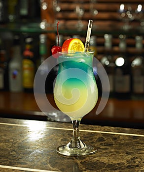 Cocktail drinks. A glass of layer cocktail with lemon and cherries, set against a bottle of alcoholic drinks at the bar