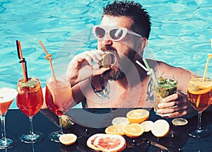 Cocktail with fruit at bearded man in pool. Man swimming and drink alcohol. Summer vacation at Miami or Maldives. Pool