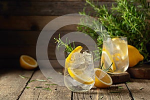 Cocktail gin tonic with ice, lemon, and rosemary on a old wooden table