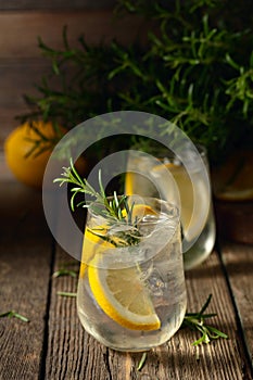 Cocktail gin tonic with ice, lemon, and rosemary on a old wooden table