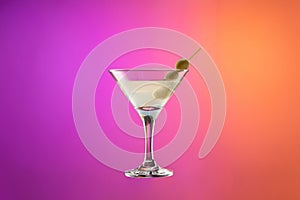 Cocktail glass with dry martini with olives isolated over gradient purple and orange color background in neon.