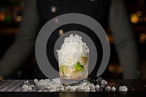 Cocktail glass filled with ice, lime and cane sugar. Process of making Caipirinha cocktail