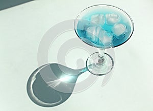 cocktail glass with ice blue water, hard shadows