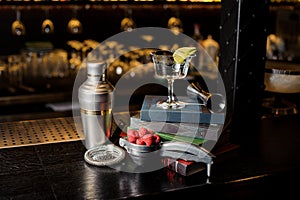 Cocktail glass with lime slice and bar utensils arranged among b