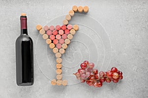 Cocktail glass with straw made of wine corks, bottle and grapes on light grey table, flat lay