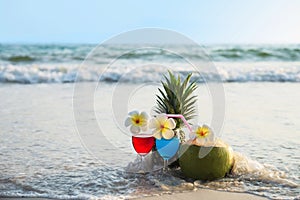 Cocktail glasses with coconut and pineapple on clean sand beach