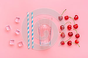 Cocktail ingredients - paper tubes with blue, white stripes, ice cubes, cherry, glass cup isolated on pink background Flat lay Top