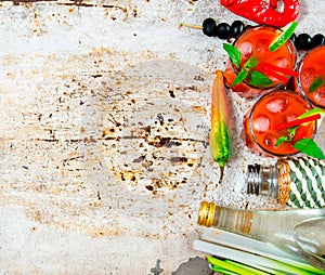 Cocktail made of tomatoes, vodka, ice, lime, pepper , salt and snack with celery and black olives on rustic background .