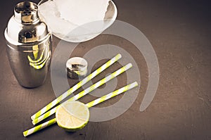 Cocktail making bar tools/Cocktail making bar tools, shaker, lime, ice and straws on a dark background. Copyspace