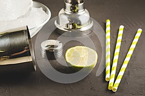 Cocktail making bar tools/Cocktail making bar tools, shaker, lime, ice and straws on a dark background. Selective focus