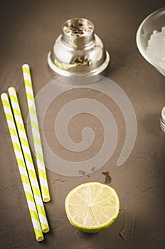 Cocktail making bar tools/Cocktail making bar tools, shaker, lime, ice and straws on a dark background. Top view and copyspace