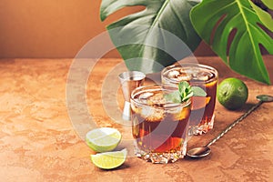 Cocktail from rum and cola ice cubes in glass glasses green leaves of a tropical plant dark brown background. S