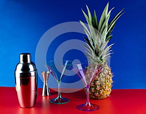 Cocktail Shaker with Cocktail Glasses and Pineapple on a Red Base and Blue Background