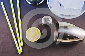 Cocktail shaker, lime, ice and straws/Cocktail shaker, lime, ice and straws on a dark background. Top view
