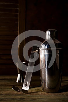 Cocktail shaker, swizzle, tongs and spoon with ice in a bucket for preparing a summer cocktail beverage on a black table