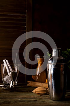 Cocktail shaker, swizzle, tongs and spoon with ice in a bucket for preparing a summer cocktail beverage on a black table