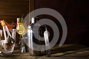 Cocktail shaker, swizzle, tongs and spoon with ice in a bucket for preparing a summer cocktail on dark background with