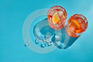 Cocktail. Two glasses with cool beverages, sliced oranges and ice on blue background with shadow. Top view with copy space