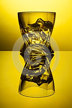 Cocktail whiskey a glass with pieces ice of party reflection a concept of hourglasses on yellow