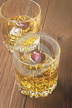 Cocktail from whisky with cherry in two glasses on a wooden back