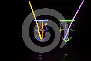 Cocktail wine glass filled with illuminated refreshing alcohol liquid and colorful straw with black background for nightlife