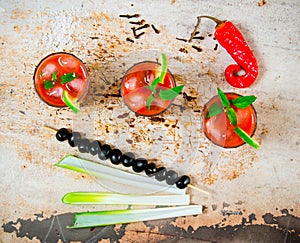 Cocktails made of tomatoes, vodka, ice, lime, pepper , salt and snack with celery and black olives on rustic background .