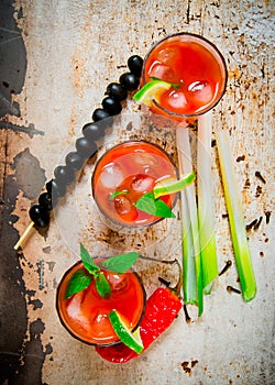 Cocktails made of tomatoes, vodka, ice, lime, pepper , salt and snack with celery and black olives on rustic background .